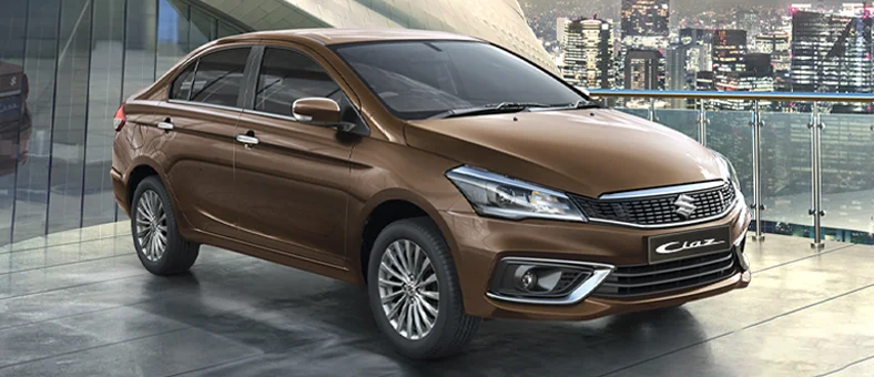 Brown Suzuki Ciaz sedan parked on a rooftop with city skyline in the background, available for rent with Selfdrive. 